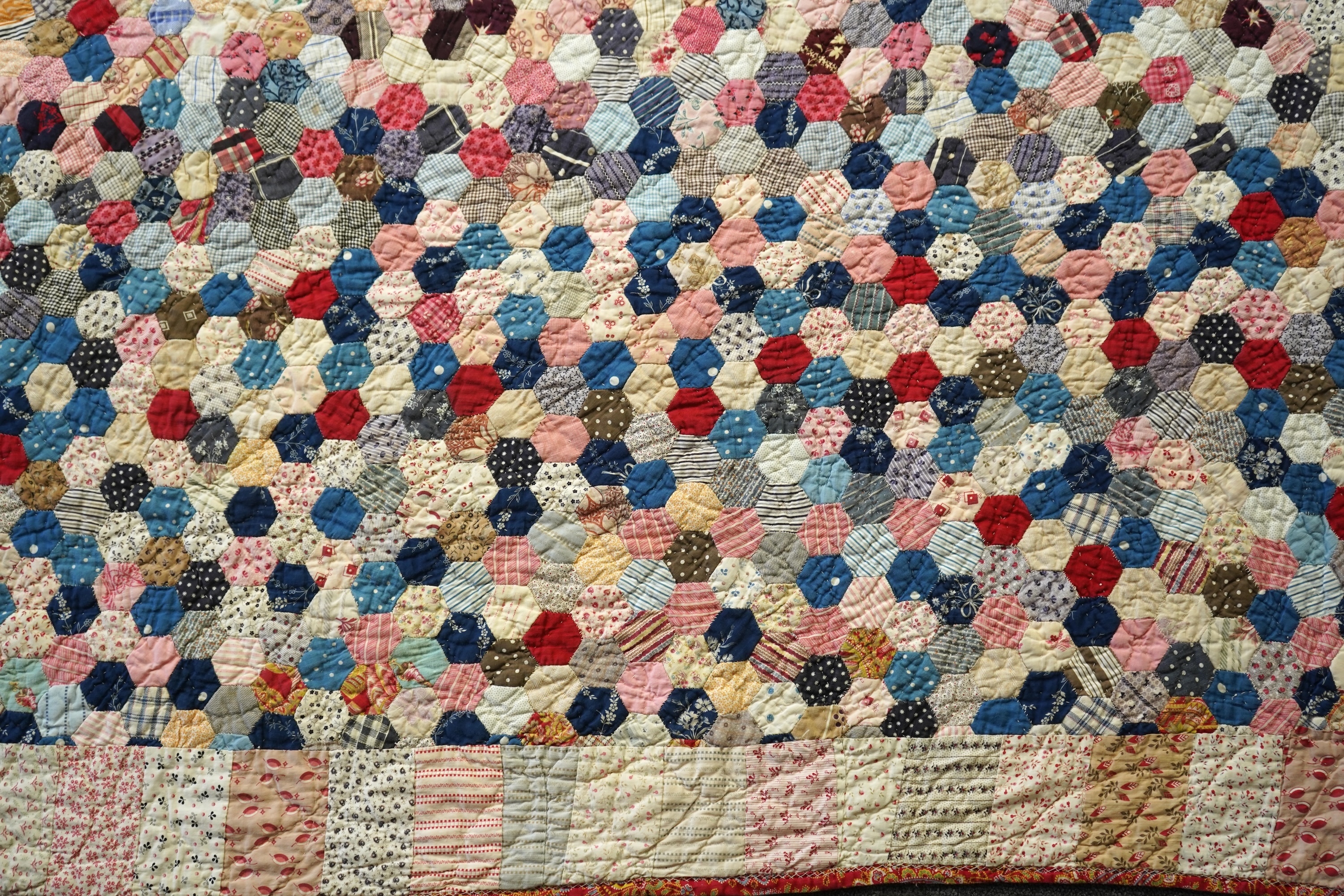 An English cotton hexagon hand made and hand pieced quilt, made from a large variety of printed dress fabrics from 19th century. The quilt edged with a wide stripped multi fabric border. The under side designed in wide s
